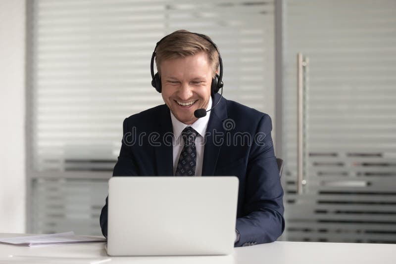 Happy smiling businessman in headset using laptop, working online, confident employee wearing suit consulting client customer or watching webinar, looking at screen, making business video call
