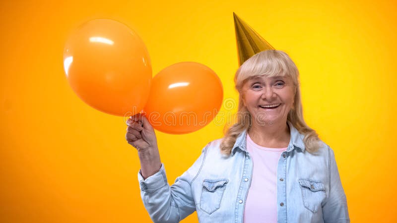 Happy smiling elderly lady holding balloons on yellow background, anniversary stock images Happy smiling elderly lady holding balloons on yellow background, anniversary stock images
