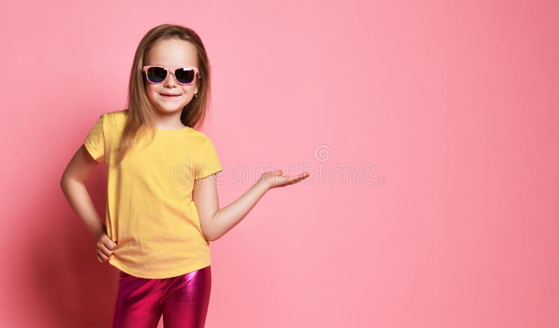 Happy smiling kid girl preschooler in yellow t-shirt and sunglasses holds hand up with open palm with free copy space