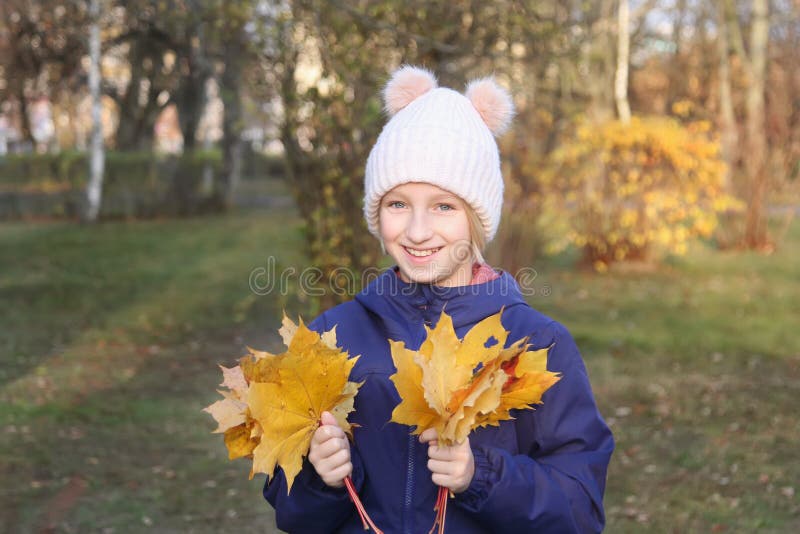 Happy smiling kid girl in a warm knitted hat collects bouquet of yellow leaves. Autumn in the park. Happy smiling kid girl in a warm knitted hat collects royalty free stock photos Happy smiling kid girl in a warm knitted hat collects bouquet of yellow leaves. Autumn in the park. Happy smiling kid girl in a warm knitted hat collects royalty free stock photos