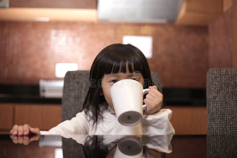 Happy smiling little Asian girl drinking a glass of milk or tea in white cup royalty free stock photos