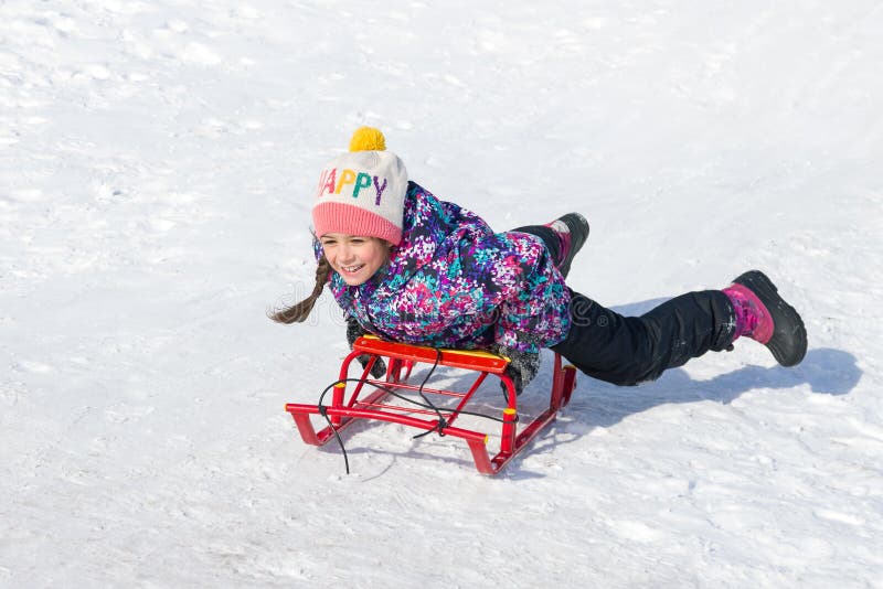 Happy smiling little girl on a sled sliding down a hill on snow