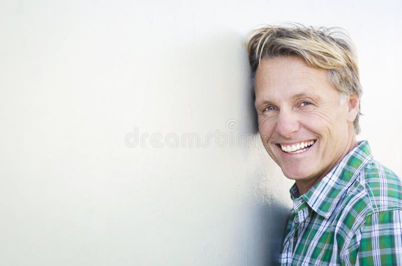 Color portrait photo of a happy laughing blond haired man in his forties wearing a green checked shirt and leaning against a white wall. Color portrait photo of a happy laughing blond haired man in his forties wearing a green checked shirt and leaning against a white wall.