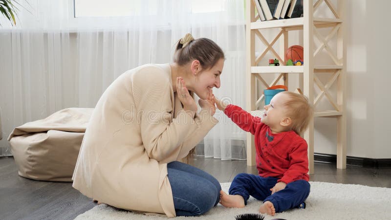 Happy smiling mother playing with her cute baby son on carpet in living room
