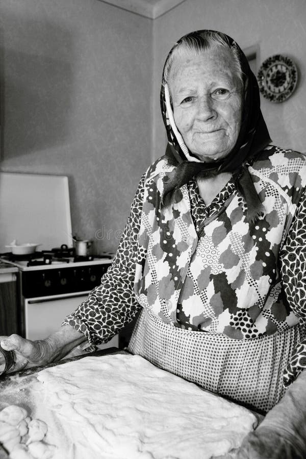 Šťastná, usmievavá starenka, stará mama, pečie, varí v kuchyni v útulnom dome. Stredoeurópska kultúra.