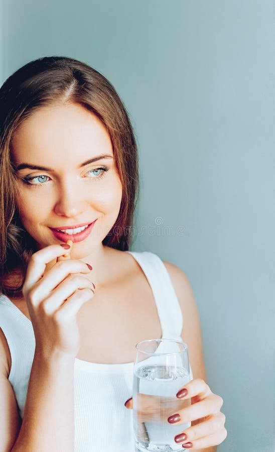 Happy smiling positive woman eating the pill and holding the glass of water in the hand. In her home royalty free stock photo Happy smiling positive woman eating the pill and holding the glass of water in the hand. In her home royalty free stock photo