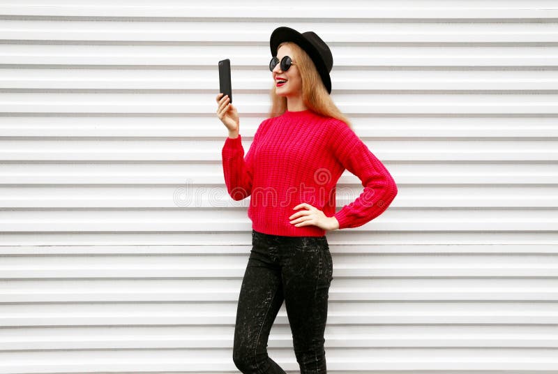 Happy smiling woman holding smartphone in colorful pink knitted sweater on city white wall royalty free stock photo Happy smiling woman holding smartphone in colorful pink knitted sweater on city white wall royalty free stock photo