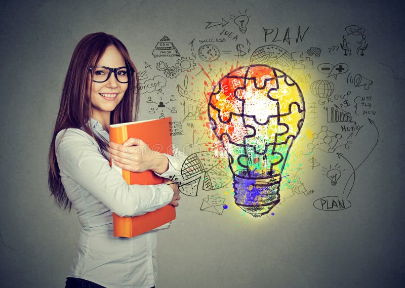 Happy smiling woman with orange folder notebook near a concrete wall with a bright puzzle light bulb business id