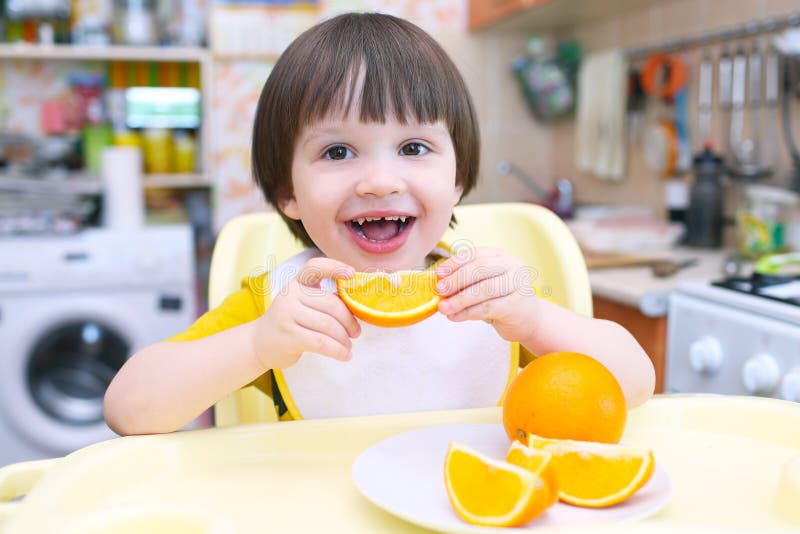 Happy smiling 2 years child eats orange