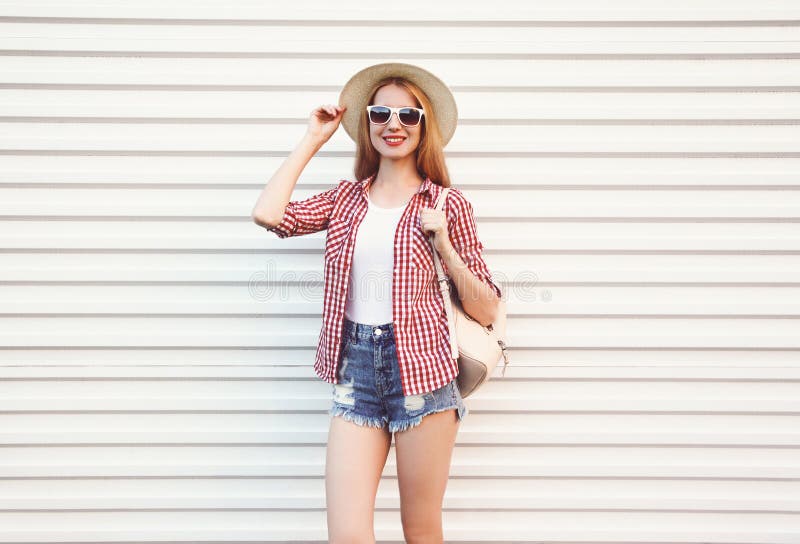 Happy smiling young woman in summer round straw hat, checkered shirt, shorts posing on white wall stock photography Happy smiling young woman in summer round straw hat, checkered shirt, shorts posing on white wall stock photography