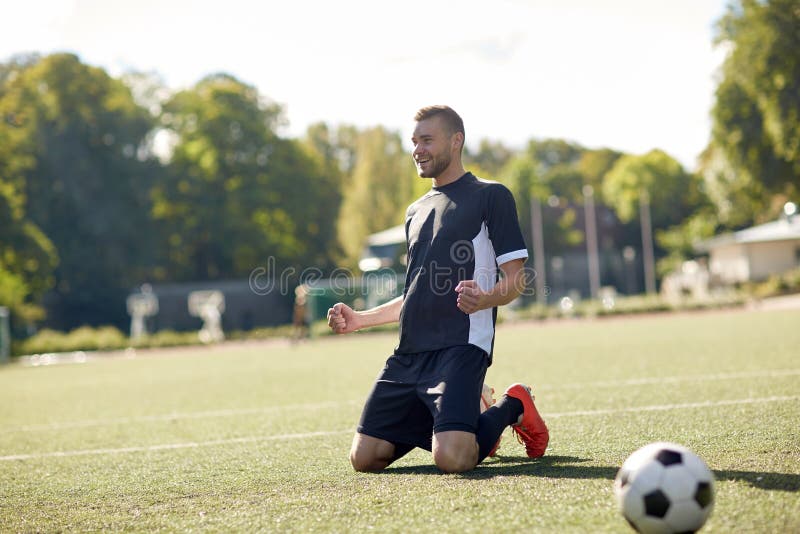 Happy soccer player with ball on football field.