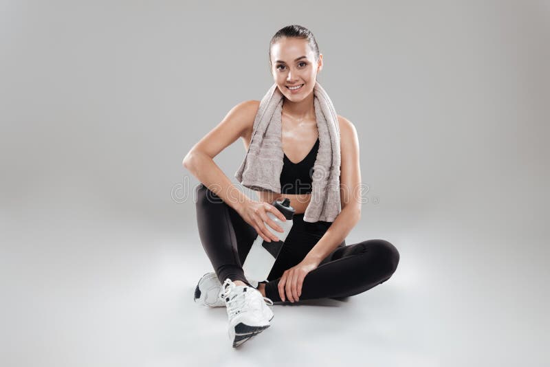 Happy sportswoman with towel sitting and holding bottle of water