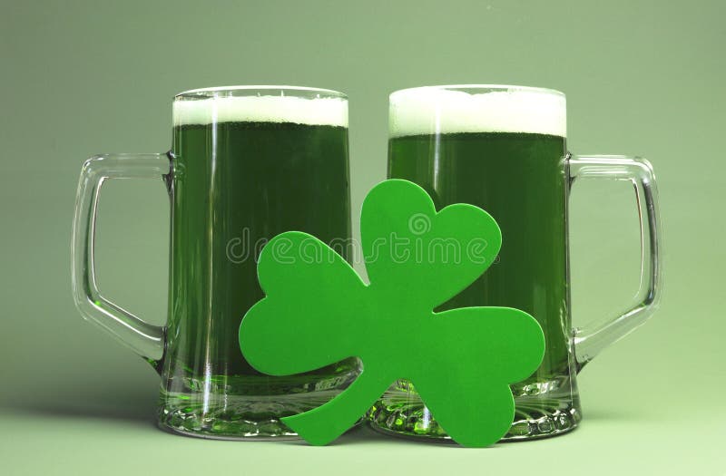 Happy St Patrick's Day celebrations with two large glass steins of green beer and Irish shamrock against a green background.