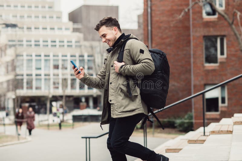 Happy student man text on cell phone walking in city college campus with backpack.