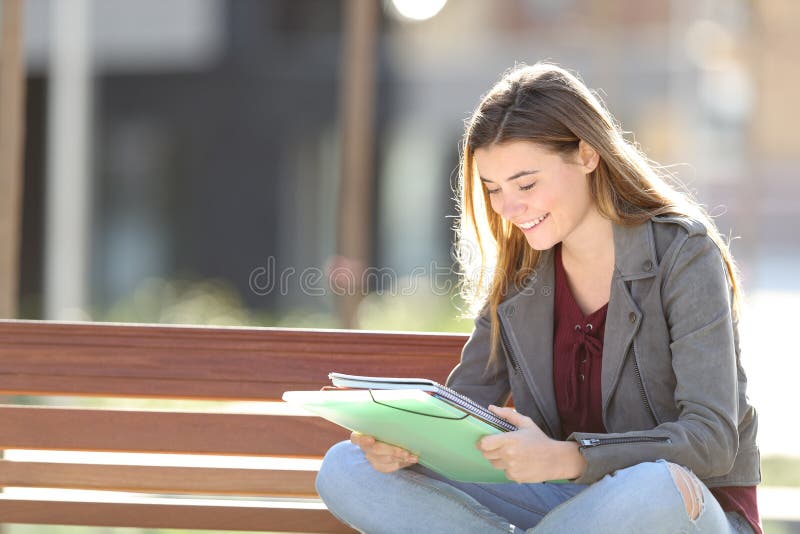 Happy student is studying reading notes sitting on a bench in a park. Happy student is studying reading notes sitting on a bench in a park