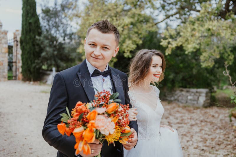 Happy stylish smiling couple walking in Tuscany, Italy on their wedding day. The bride and groom walk down the street by