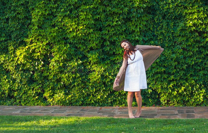 Happy stylish women hipster boho style dancing near green leaves wall building in sunny city, summer travel, nature love concept.