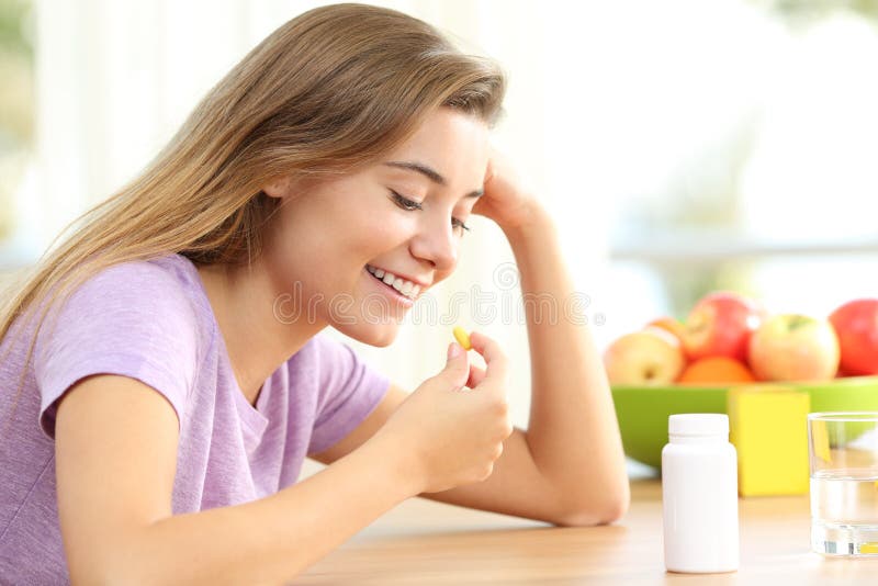 Happy teen taking a vitamin pill at home. Happy teen taking a omega 3 vitamin pill on a table at home royalty free stock images Happy teen taking a vitamin pill at home. Happy teen taking a omega 3 vitamin pill on a table at home royalty free stock images