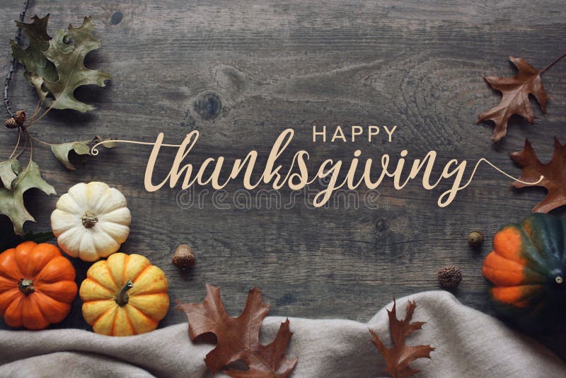 Happy Thanksgiving typography with pumpkins and leaves over dark wood background