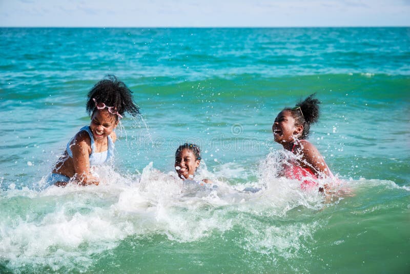 Happy three African American kids are swimming in the sea playfully together. With waves and splashes of water. Happy friendship. Happy vacation holiday. Relaxation in vacation in the summer concept