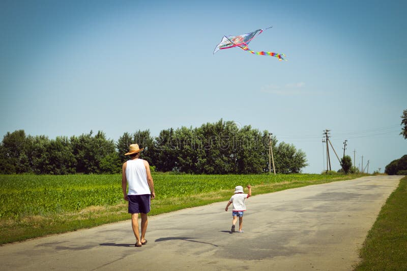Happy times: image of father & son having fun playing with kite outdoors on summer sunny day green woods & blue sky