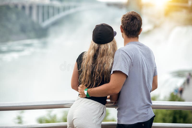 Happy tourist couple enjoying the view to Niagara Falls during romantic vacation. People looking to nature landscape at sunset tim