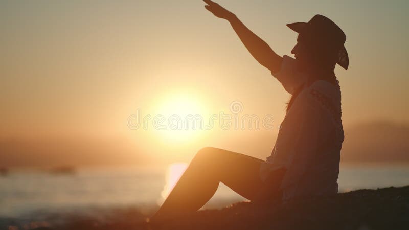 Happy travel girl relaxing on beach throwing pebble into sea at big yellow sun background