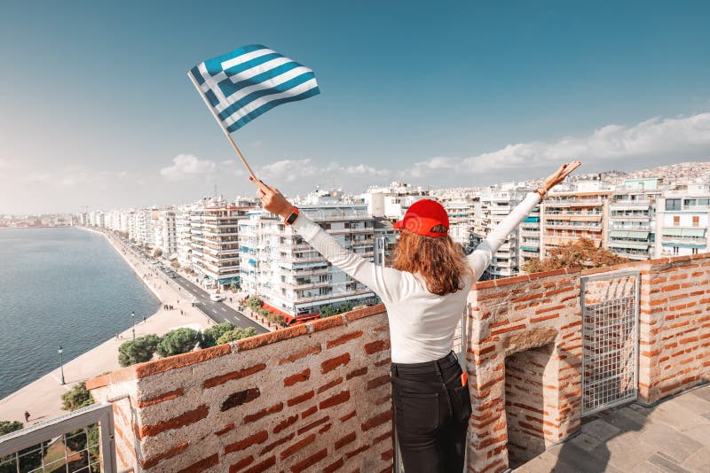 Traveller girl with flag on the top viewpoint of a White Tower in Thessaloniki. The concept of citizenship or learning Greek