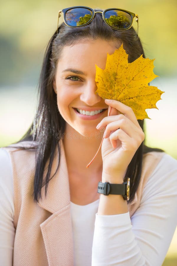 Happy woman with beautiful smile holds yellow autumn leaf.