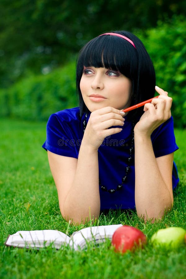 Happy young woman writing in book in countryside with ripe apple, green nature background. Happy young woman writing in book in countryside with ripe apple, green nature background.
