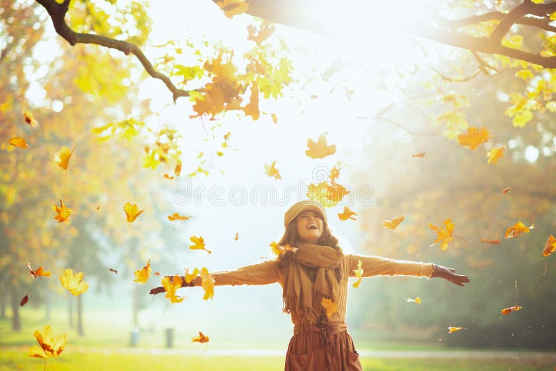 Happy woman enjoying autumn and catching falling yellow leaves