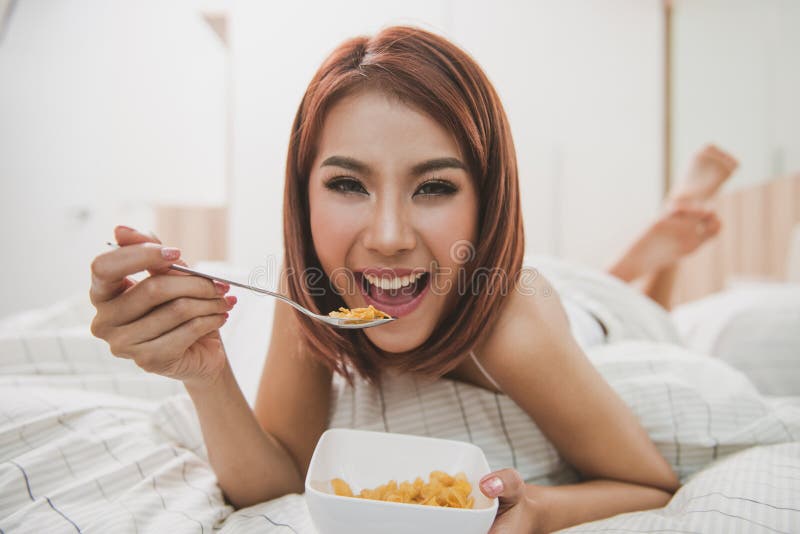 Happy woman enjoying cornflakes cereals in the bed in the morning. Happy woman enjoying cornflakes cereals in the bed in the morning.