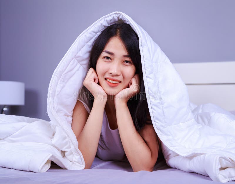 Happy woman hiding under blanket on bed in bedroom royalty free stock photo