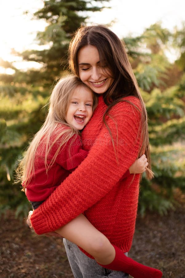 Happy woman hold little kid girl 3-4 year old wear red bright sweaters posing over nature