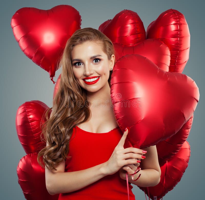 Happy woman holding balloons red heart. Surprise, valentines people and Valentine`s day concept. Red lips makeup.