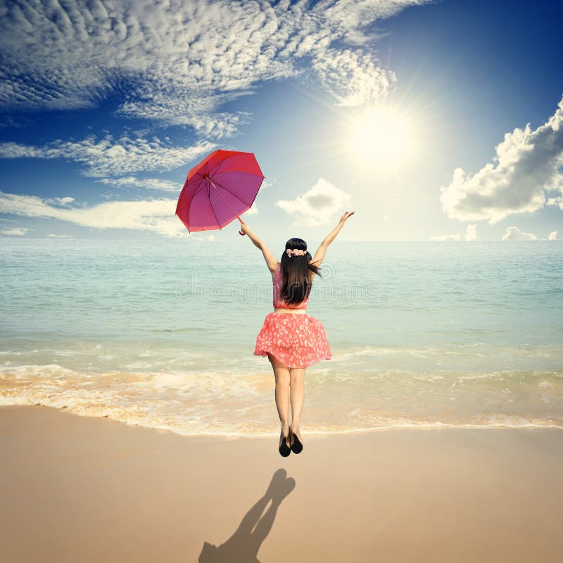 Happy Woman holding umbrella and Jumping in Sea sun sky