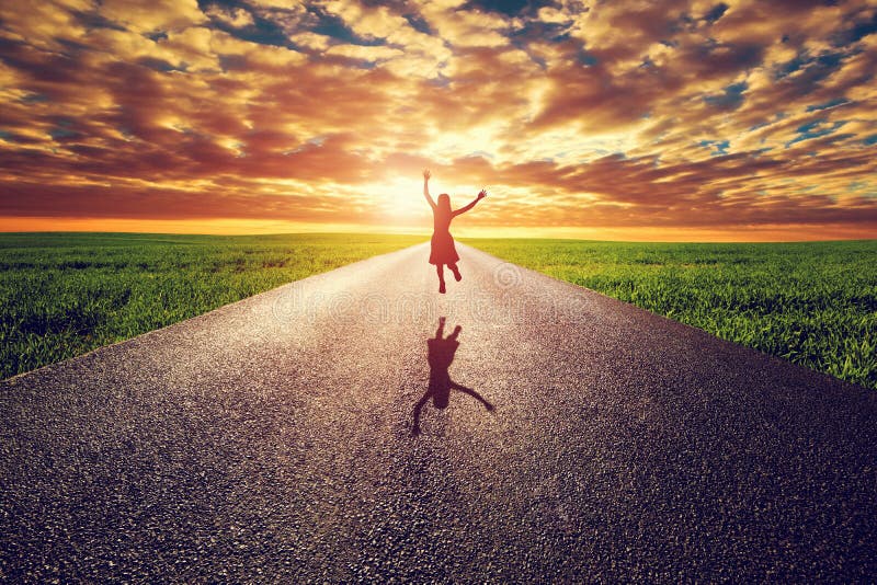 Happy woman jumping on long straight road, way towards sunset sun