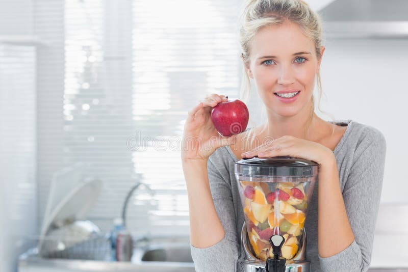 Happy woman leaning on her juicer full of fruit and holding red apple stock images Happy woman leaning on her juicer full of fruit and holding red apple stock images