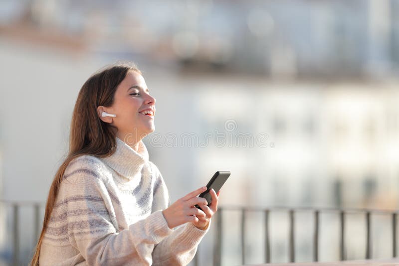 Happy woman listens to music with wireless earbuds in a balcony royalty free stock images Happy woman listens to music with wireless earbuds in a balcony royalty free stock images