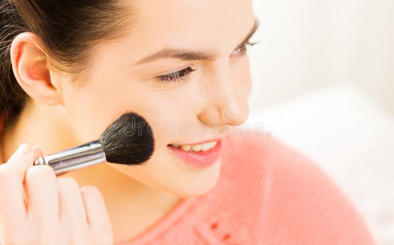 Happy woman with makeup brush blushing cheekbone.