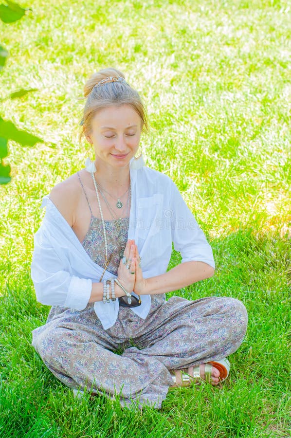 Happy woman is meditating sitting in Lotus pose on grass. Beautiful boho style woman with accessories enjoying sunny day in park royalty free stock photos Happy woman is meditating sitting in Lotus pose on grass. Beautiful boho style woman with accessories enjoying sunny day in park royalty free stock photos