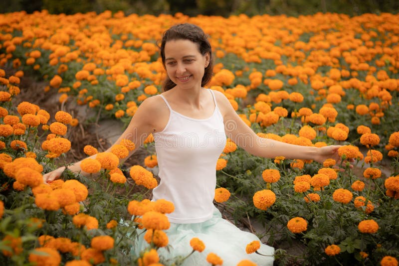 Young Caucasian woman seating among marigolds and touching flowers. Marigold valley in Bali. Happy woman sitting among marigolds and touching flowers. Marigold stock photography Young Caucasian woman seating among marigolds and touching flowers. Marigold valley in Bali. Happy woman sitting among marigolds and touching flowers. Marigold stock photography