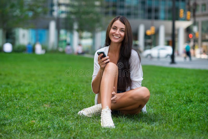 Happy woman sitting on green grass at city park and using smartphone stock images Happy woman sitting on green grass at city park and using smartphone stock images