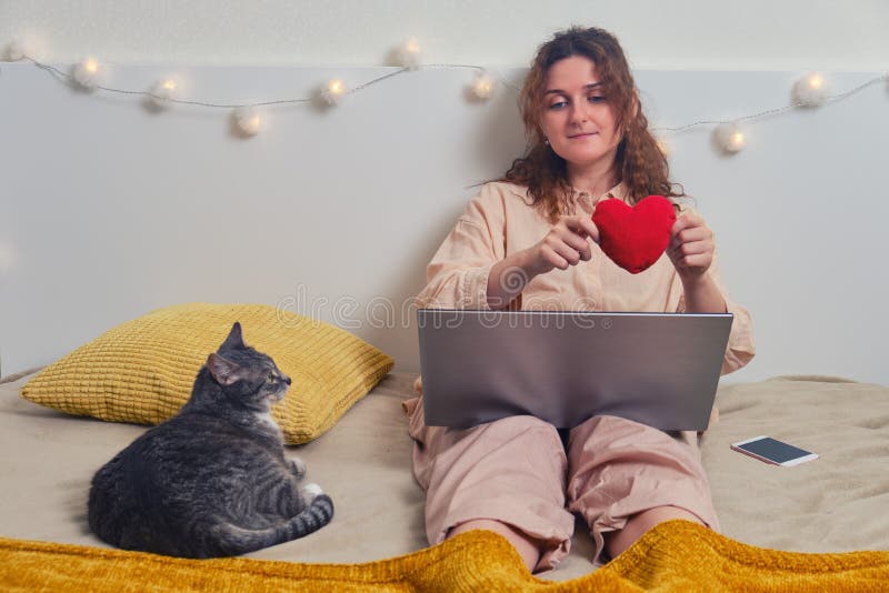 Happy woman is texting on online dating sites. Girl sitting with cat in home bedroom, internet love concept