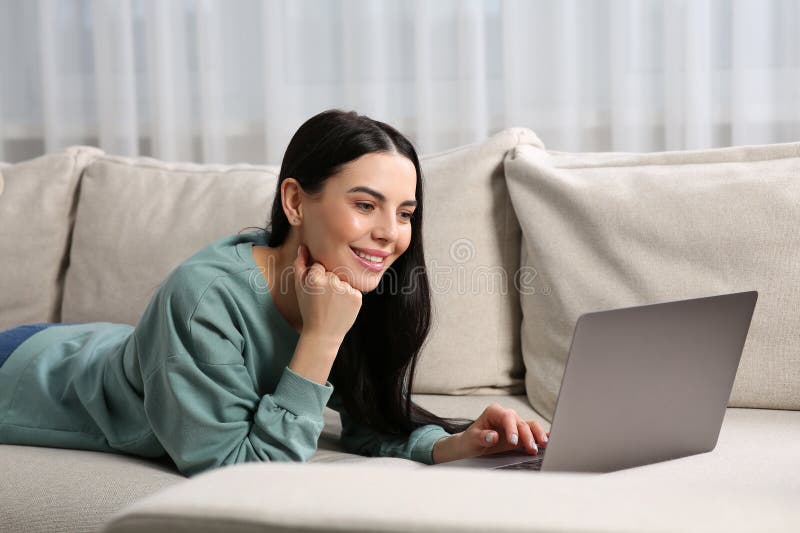 Happy woman working with laptop on sofa at home stock image