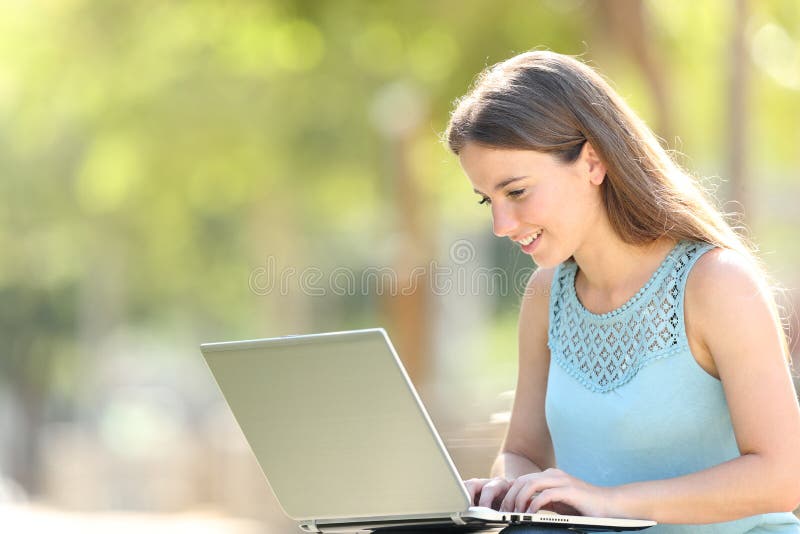 Happy woman writing on a laptop sitting in a park royalty free stock images Happy woman writing on a laptop sitting in a park royalty free stock images