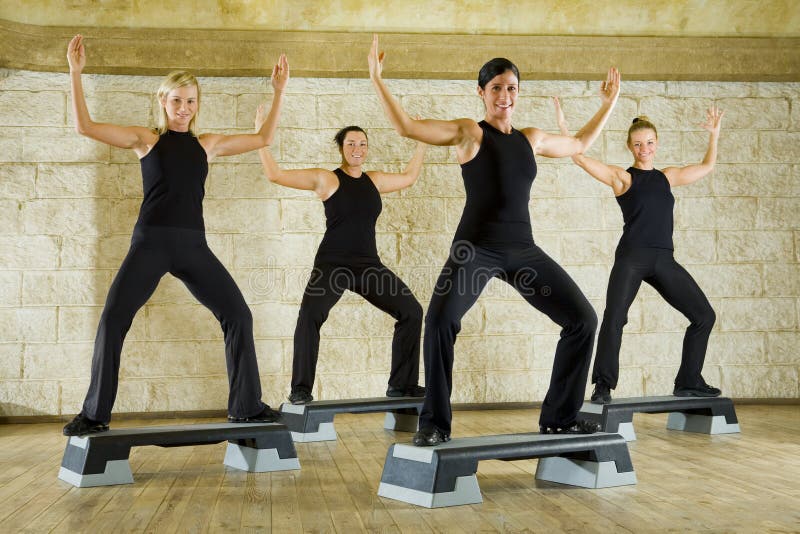 A group of women exercising in the fitness club. They're smiling and looking at camera. They have hands up. Low angle view. A group of women exercising in the fitness club. They're smiling and looking at camera. They have hands up. Low angle view.