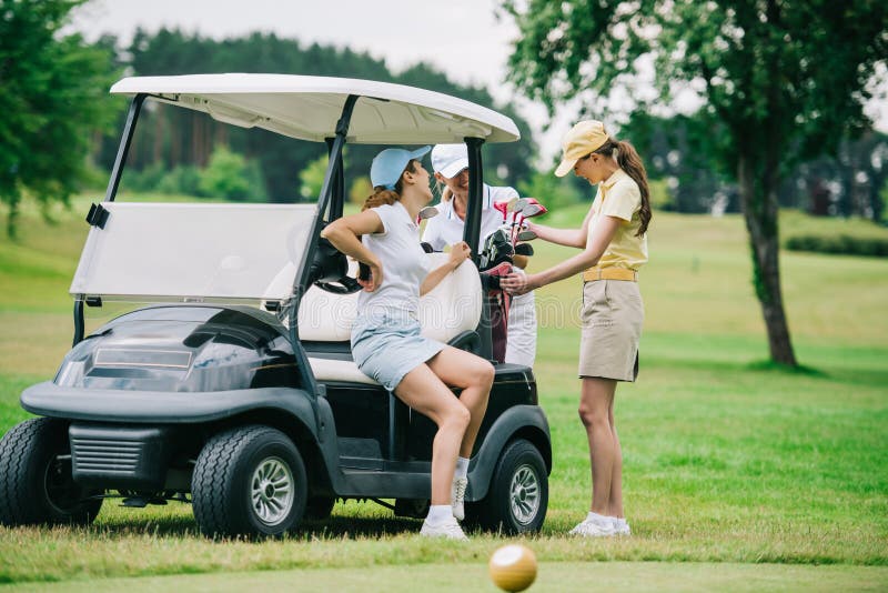 happy women in polos and caps at golf cart getting ready royalty free stock...
