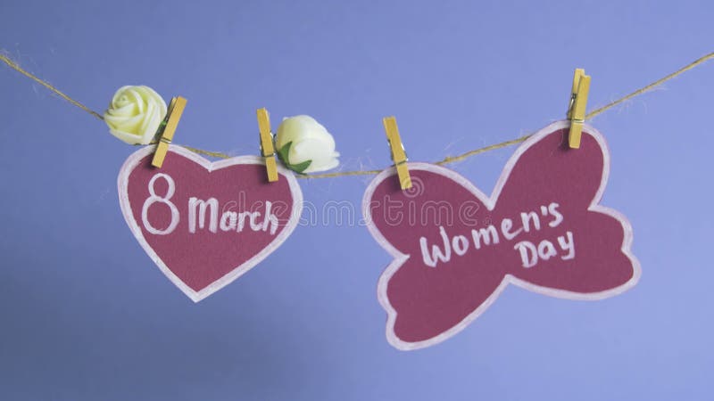 Happy Women`s Day. Women`s Day on pink paper, hanging on a rope near a pink heart decorated with flowers. Blue