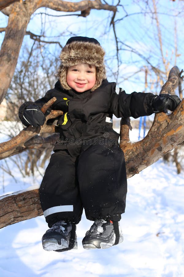 Happy 2 year toddler sitting on tree in winter stock image